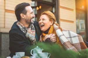 midle-aged couple laughing and leaning into each other at an outdoor cafe